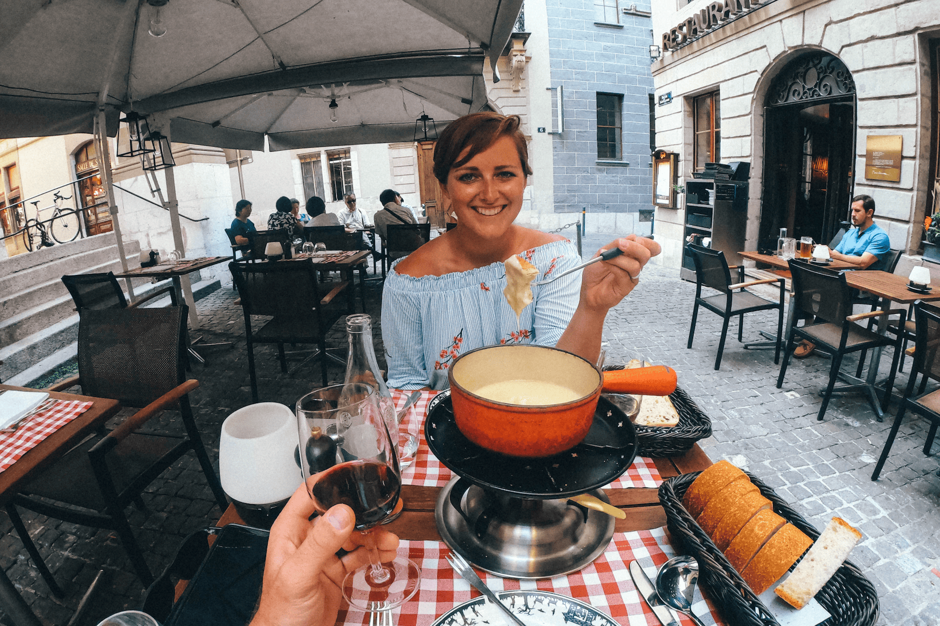 A woman sitting at a restaurant eating cheese fondue with gluten free bread on the side. 